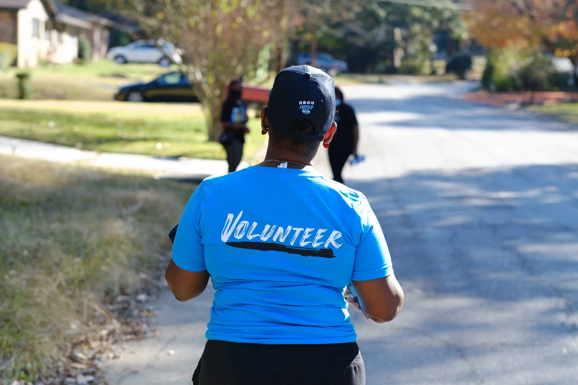 A BlackPAC volunteer in a Volunteer shirt walking down a neighborhood street