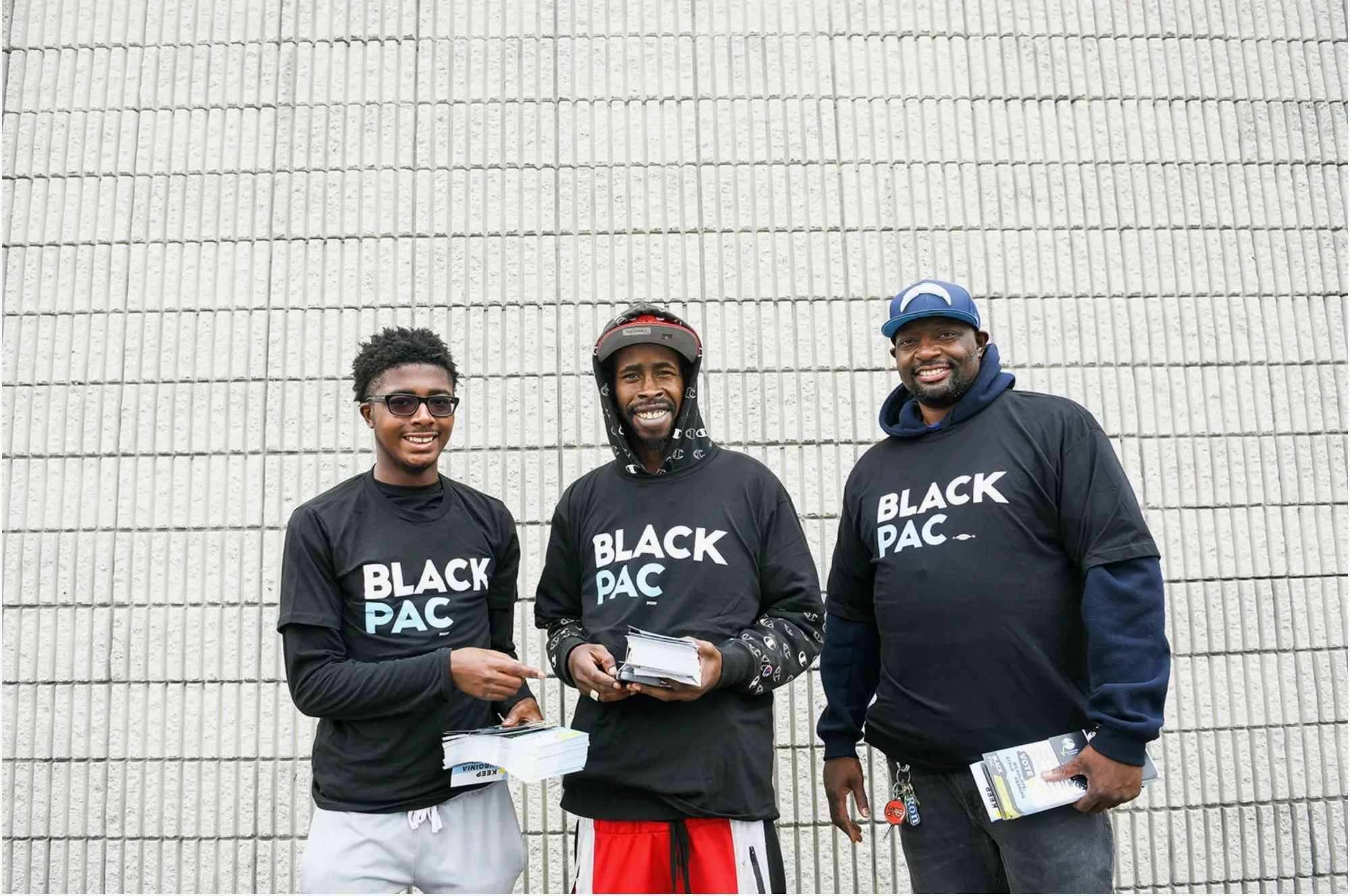 Three BlackPAC volunteers in BlackPAC shirts holding stacks of voter guides